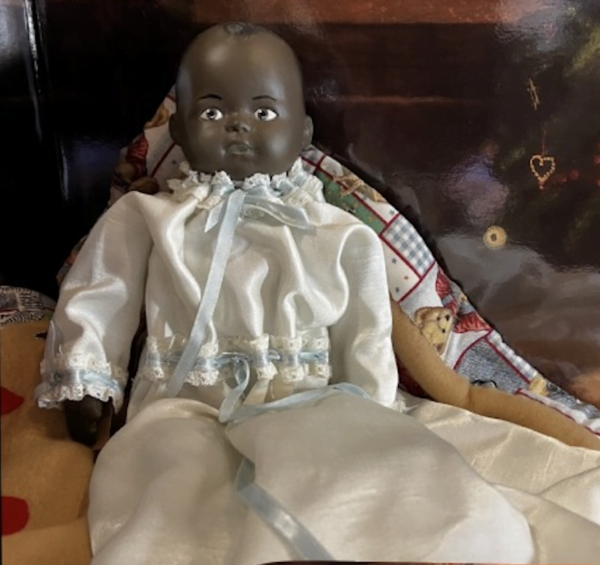A close-up of Brenda, a 12-inch oil cloth doll, wearing a Victorian-inspired white dress with lace and blue ribbon accents. Her hand-painted features exude charm and grace.